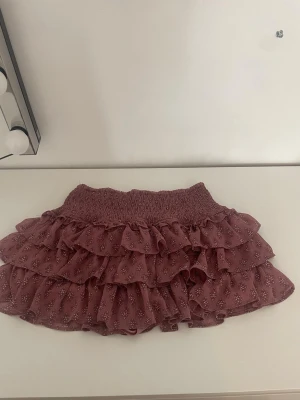 Rosa volangkjol med småblommigt mönster - Supersöt kortkjol med shorts i mörkrosa med småblommigt mönster och flera lager volanger. Kjolen har bred resår i midjan för skön passform och är gjord i ett lätt, luftigt material som passar perfekt till varmare dagar.