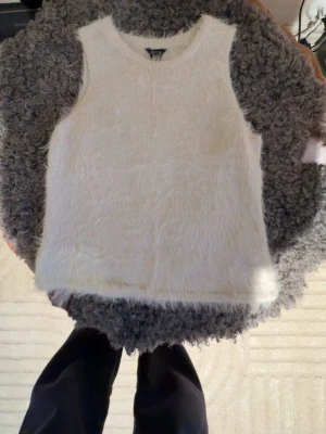 Vit fluffig ärmlös tröja Lindex - Supersnygg vit stickad ärmlös tröja från Lindex. Tröjan har en fluffig, mjuk yta och rund halsringning. Storlek M men passar även S super bra. Perfekt att styla med ett par jeans för en trendig look.