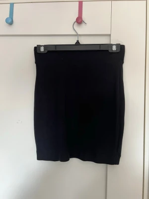 Svart tight kortkjol - En enkel och stilren svart kortkjol med tight passform. Kjolen är rak i modellen och passar perfekt till både vardags- och partylooks. Tillverkad i mjukt material som ger en bekväm känsla hela dagen.