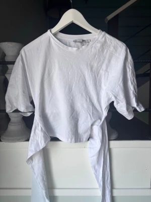 Vit croppad topp med knyt - Säljer en vit croppad topp med korta ärmar och knytband i midjan. Toppen har en enkel och clean design. Skriv för fler bilder. Tvättar såklart innan jag postar❣️aldrig använt 