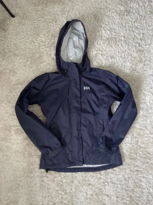 Jacka Helly Hansen  - Marinblå regnjacka/vindjacka ifrån Helly Hansen. Storlek xs och i superbra skick bortsett från några små fläckar (se bilder). Den har fickor på både utsida och insida och även dragkedjor under armarna. Hör av dig om du har några frågor 💗