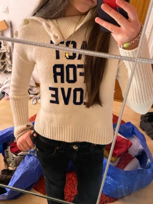 Zadig & Voltaire tröja | Strl 11-12 | vit/beige | - Elegant Zadig & Voltaire-tröja i beige/vit nyans med blå text “Act for Love” framtill. Modell med lång hals och dekorativa knappar, vilket ger en stilren och feminin look. I mycket fint skick, inga defekter. Perfekt både till vardag och mer uppklädda tillfällen. Strl 11-12 dock är den för liten på mig som är nära den åldern, syns på bild. Jag är ca 152cm!       Tröjan är kanske krympt tyvärr…