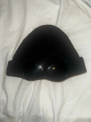 Svart mössa med glasögon från C.P. Company - Svart CP mössa köpt på miinto använda i ett jätte bra skick en gammal modell men givetvist äkta kolla certilogo koden pris kan diskuteras 