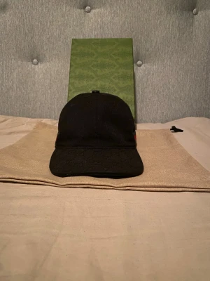 Svart keps från Gucci med GG-mönster - Snygg svart keps från Gucci med det klassiska GG-monogrammönstret över hela kepsen. Kepsen har böjd skärm och justerbar rem bak. Perfekt accessoar för en trendig och exklusiv look.