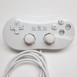 Vit Wii Classic Controller handkontroll - Wii Classic Controller i vit färg.   Ansluts till Wii Remote. Kontrollen är trådbunden och har en anslutning som passar Wii Remote.  Tredjepartstillverkad