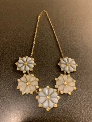 Blommigt statementhalsband i guld, H&M - Snyggt halsband med stora blommor i mintgrön och ljusrosa, dekorerat med gnistrande stenar. Kedjan är guldfärgad och blommorna har en cool, retro känsla. Perfekt för att lyfta vilken outfit som helst med lite extra bling.
