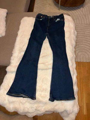 Mörkblå bootcut jeans från 157 - Säljer ett par mörkblå bootcut jeans från 157 med klassiska orange sömmar och femficksmodell. Jeansen har en snygg utsvängd passform nedtill och är tillverkade i mjukt denimtyg. Perfekta för dig som gillar retrovibbar och vill ha ett par bekväma jeans.