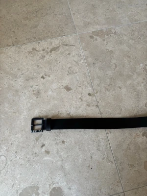 Svart läderbälte från Replay - Säljer ett svart bälte från Replay i äkta skinn. Bältet har en klassisk rektangulär metallspänne med Replay-logga och flera hål för justering. Perfekt accessoar för att lyfta din outfit. Knappt använt alls Nypris 599kr mitt pris 349kr
