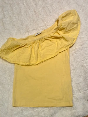 Gul off shoulder topp med volang - Trendig gul off shoulder topp från kappahl med bred volang runt halsen. Tillverkad i mjukt bomullsmaterial som känns skönt mot huden. Perfekt för dig som vill ha en färgglad och somrig look.