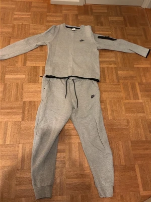 Gråa mjukisbyxor från Nike - Säljer ett par gråa mjukisbyxor från Nike med dragsko i midjan och muddar vid bensluten. Byxorna har en avslappnad passform och passar perfekt för extra mysiga kvällar eller mestadels för en chill outfit Byxorna är i storlek M och tröjan i S i barnstorlek. Kan säljas separat också, hör av er i DM vid intresse, men även vid diskutering av lägre pris!