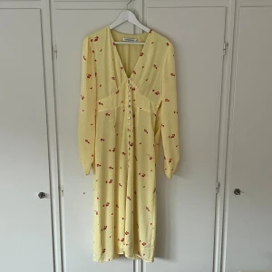 Adoore Paris dress, storlek 40 - Säljer min superfina Paris dress från från Adoore i ljusgul ton med små röda blommor. Klänningen har v-ringning, långa ärmar och knappar framtill. Klänningen är helt oanvänd! Den är i storlek 40 men passar även en 38 ❣️Nypris 1495 kr❣️