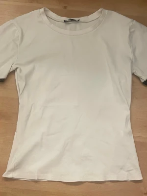 Vit t-shirt med glittriga ärmslut - En stilren vit t-shirt med korta ärmar och rund hals. Ärmsluten har en snygg glittrig kant i svart som ger en extra detalj. Perfekt till jeans eller kjol för en enkel och basic look.
