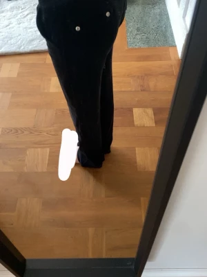 Svarta mjukisbyxor juicy couture - Säljer ett par svarta mjukisbyxor i mjuk velour med raka ben och dragsko i midjan. Byxorna har fickor med silverfärgade knappar framtill och en avslappnad passform. Perfekta för en chill och bekväm stil.