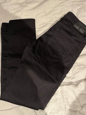 Svarta slim fit jeans tiger of sweden - Säljer ett par svarta slim fit jeans med klassisk femficksdesign och svarta sömmar. Jeansen har en svart läderpatch bak i midjan och är tillverkade i ett mjukt bomullsmaterial med lite stretch för extra komfort. Perfekta till en avslappnad streetwear-look.