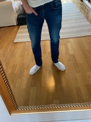 Mörkblå slim fit jeans - Säljer ett par mörkblå slim fit jeans med snygga slitningar och tvättade detaljer. Jeansen har klassisk femficksmodell, smal passform och normal midja. Materialet är stretchigt denim som ger en bekväm känsla och följer kroppen. Perfekta för en trendig och avslappnad stil. Köpte för runt 1700kr