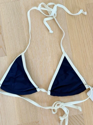 Marinblå trekantsbikini med vita band - Snygg trekantsbikini i marinblått med vita kanter och knytband. Klassisk och stilren modell som knyts i nacken och ryggen. Perfekt för lata dagar på stranden eller poolen.