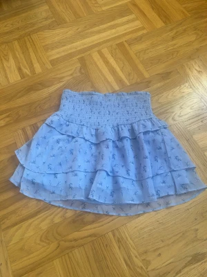 Ljusblå volangkjol med blommönster från Gina tricot💕💕💕 - Säljer en ljusblå kortkjol med volanger och små blommor från Gina tricot💕💕💕. Kjolen har bred smock i midjan för skön passform och är gjord i ett lätt, luftigt material som passar perfekt till varma dagar💕💕💕💕💕I mycket bra skick💕💕Jag säljer den för 75 kr💕💕Hör av er vid intresse💕💕💕💕