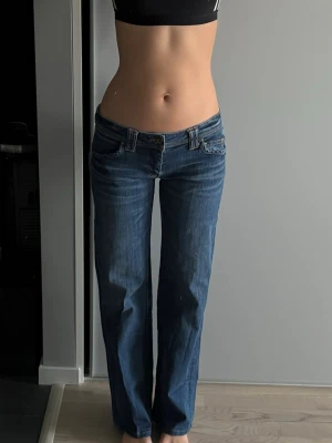 Blå bootcut jeans med fickdetaljer - Säljer ett par blå bootcut jeans med låg midja och snygga fickdetaljer bak med knapp. Jeansen har klassisk femficksdesign och är tillverkade i denim med lätt tvättad look. Perfekta för en avslappnad och trendig stil. Köpte secondhand super bra kavlite jag är 167 💓