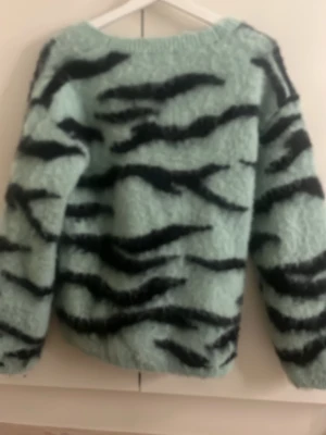 Monki mintgrön fluffig kofta - Supermjuk och fluffig kofta från Monki i mintgrönt med svart zebramönster. Koftan har v-ringning, knäppning framtill och ribbade muddar vid ärmslut och nederkant. Perfekt för dig som gillar statementplagg och djurmönster.