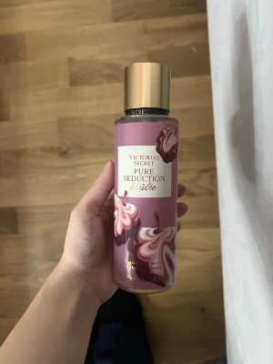 Victoria's Secret Pure Seduction Brûlée - En snygg parfymmist från Victoria's Secret i doften Pure Seduction Brûlée. Flaskan är lila med guldigt lock och dekorerad med krämiga, rosa och vita mönster. Perfekt för dig som gillar söta och fräscha dofter i en stilren plastflaska.
