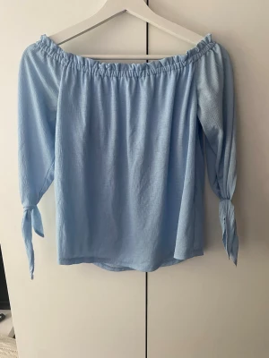 Ljusblå offshoulder-blus med knytärmar -  Ljusblå offshoulder-blus med knytband vid ärmsluten☺️jättefin men säljer då jag bara inte fått användning för den