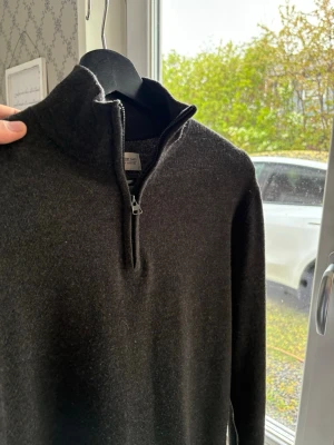 Mörkgrå halvzip-tröja these glory days - Mörkgrå stickad tröja från these glory days med halv dragkedja och hög krage. Tröjan har lång ärm och är gjord i mjukt material som ger en clean och stilren look. Perfekt för lager-på-lager och funkar året runt.