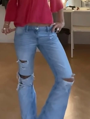 Ljusblå slitna bootcut jeans - Säljer ett par ljusblå bootcut jeans med flera slitningar och hål på benen då de tyvärr inte används💕 Jeansen har en unik detalj med en mörkblå bakficka och en ljusblå bakficka med slitningar. Tillverkade i denim med klassisk knappgylf. Pris kan diskuteras!