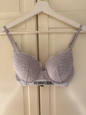 Ljuslila spets-bh från Victoria's Secret - Supersnygg ljuslila bh från Victoria's Secret med vadderade kupor och bred resår med logga. Bh:n har justerbara axelband och är täckt av ett detaljerat spetsmönster som ger en lyxig känsla. Perfekt för dig som gillar både komfort och stil.