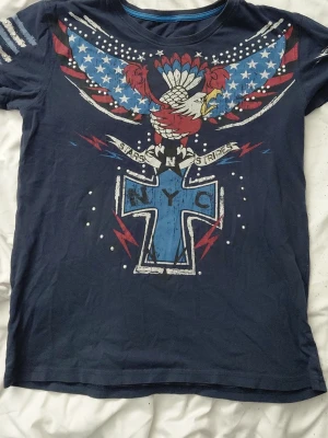 Mörkblå t-shirt med USA-tryck - Cool mörkblå t-shirt. Nån paljett saknas men de märks inte. Lappen är avklippt så jag vet tyvörr ej vart den är ifrån. Skulle gissa på att storleken är S-M ä. Märket jag sätter stämmer INTE