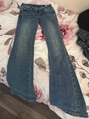 Blå utsvängda jeans med låg midja - Säljer ett par blå jeans med riktigt utsvängda ben och låg midja. Klassisk femficksmodell i denim med slitningar framtill. Perfekta för dig som gillar retro eller 00-talsstil. Materialet är bomullsdenim.