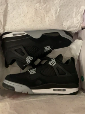 Air Jordan 4 black canvas - Snygga Air Jordan 4 sneakers i svart med grå och vita detaljer. Klassisk siluett med meshpaneler och ikoniska plastdetaljer vid snörningen. Sulan har synlig Air-enhet och skon är tillverkad i en mix av läder och textil. Perfekt för dig som gillar streetwear och basketstil. Helt nus