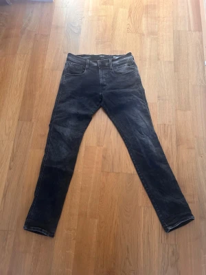 Svarta slim fit jeans från Replay - Snygga svarta jeans från Replay, modell Anbass Hyperflex med slim fit-passform. Jeansen har klassisk femficksdesign, stretchigt material och diskreta slitningar för en cool look. Perfekta för dig som gillar en smal siluett och bekväm känsla. Nypris 1700kr
