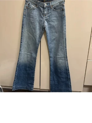 Blå bootcut jeans från 7 For All Mankind - Säljer ett par klassiska blå bootcut jeans från 7 For All Mankind. Jeansen har fem fickor, snygga slitningar och kontrastsömmar. Materialet är mjukt denim med lätt stretch. Perfekta för dig som gillar retrovibbar och en avslappnad look.