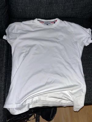 Vit Moncler t-shirt i bomull - Säljer en klassisk vit t-shirt från Moncler med diskret logotyp på bröstet. T-shirten har rund halsringning och korta ärmar. Tillverkad i mjuk bomull för en skön och stilren look.