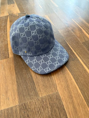 Mörkblå Gucci keps  - Snygg mörkblå keps från Gucci med det klassiska GG-monogrammet över hela kepsen. Kepsen har böjd skärm och är tillverkad i ett slitstarkt tygmaterial. Perfekt accessoar för dig som vill ha en exklusiv och trendig look.