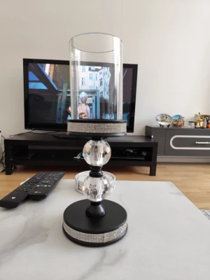 Elegant ljuslykta med kristalldetaljer - Säljer en snygg ljuslykta med svart bas och cylinderformat glas. Ljuslyktan har två stora, slipade kristallkulor och dekoreras med glittrande strassband runt både fot och topp. Perfekt som dekoration i vardagsrummet.