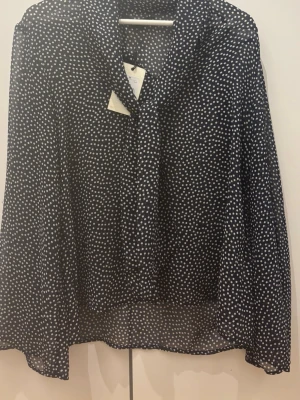 Mörkblå prickig blus med knytband - Snygg mörkblå blus från Bik Bok med vita prickar och knytband vid halsen. Blusen har långärmad design och är tillverkad i ett lätt, luftigt material som ger en avslappnad och trendig look.