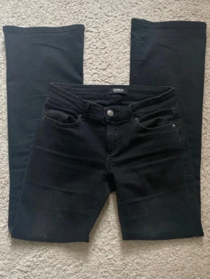 Svarta bootcut jeans från ONLY - Snygga svarta bootcut jeans från ONLY med klassisk femficksmodell och normalhög midja. Jeansen har utsvängda ben och är tillverkade i ett stretchigt denimtyg som sitter bekvämt. Perfekta för en trendig och avslappnad stil.