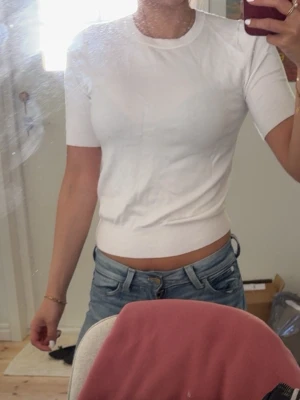Vit ribbad kortärmad topp - Snygg vit topp med ribbad nederkant och korta ärmar. Modellen är figurnära och har en klassisk rund halsringning. Perfekt att matcha med jeans eller kjol för en clean look.