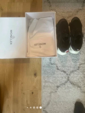 Svarta Moncle sneakers med vit sula - Snygga svarta sneakers från Moncle med chunky vit sula och klassisk logga på insidan. Skorna har svarta skosnören och en röd detalj på hälen. Kommer med originalkartong och dustbag. Perfekta för dig som gillar exklusiva och trendiga sneakers.