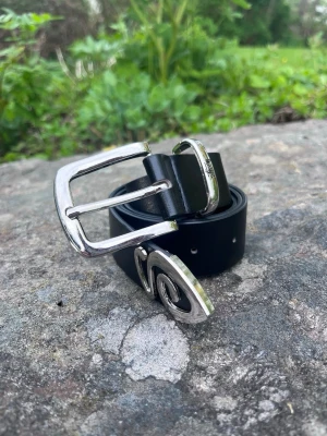Stussy bälte - Snyggt svart skärp från Stussy i äkta skinn med silvrigt spänne och Stussy-logga ingraverad på metallöglan. Perfekt accessoar för att lyfta din outfit med en clean och stilren look.