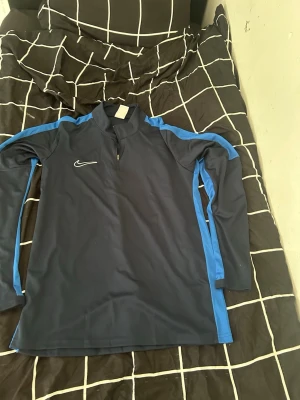 Nike Quarter Zip träningströja blå/svart – Storlek L – Helt ny - Säljer en stilren Nike Quarter Zip träningströja i blå/svart färg. Storlek L och helt ny utan prislapp. Perfekt för gym, fotboll, löpning eller vardagsstil. Tröjan har bekväm passform, dragkedja vid halsen och snygga detaljer längs armarna som ger en clean och sportig look.  Perfekt för både träning och streetwear outfits.  💰 Pris kan diskuteras vid snabb affär 📦 Fraktar samma dag vid snabb betalning