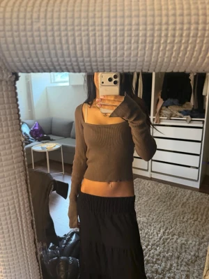 Brun ribbad croppad topp - Trendig brun croppad topp med långa ärmar och fyrkantig ringning. Toppen är ribbad och har en slim passform som framhäver figuren. Perfekt för att skapa en stilren och modern look.