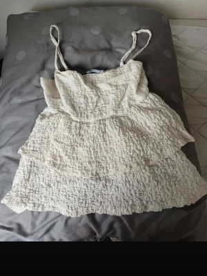 Krämvit linnetopp från Gina Tricot - Supersöt krämvit linnetopp från Gina Tricot med smala axelband och volangig struktur. Toppen har en rynkad, texturerad yta och är perfekt för varma dagar. Lätt och luftig känsla, passar till jeans eller kjol.