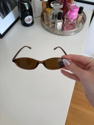 Bruna smala solglasögon i retrostil - Snygga smala solglasögon med bruna bågar och bruna glas. De har en retroinspirerad, oval form som ger en cool vibe till din outfit. Perfekta för soliga dagar och en trendig look.