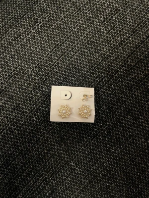 Guldiga örhängen med pärldetaljer - Snygga örhängen i guldton med stjärnformad design och små vita pärlor. Perfekta för att ge din look lite extra bling. Passar dig som gillar unika och trendiga accessoarer.