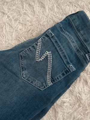 Blå jeans från Nelly med broderad ficka - Snygga blå jeans från Nelly nästan som nya, storlek 32 o är uppsydda noggrant o passar nån runt 160