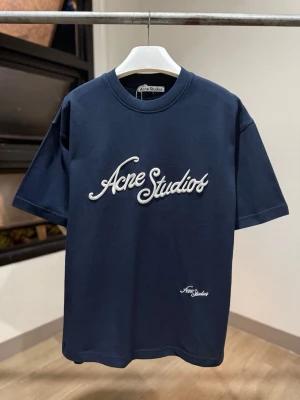 Mörkblå Acne Studios t-shirt - Snygg mörkblå t-shirt från Acne Studios med vit broderad logga framtill. Klassisk passform med rund hals och korta ärmar. Perfekt för en stilren och trendig look.