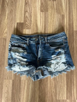Blå jeansshorts från American Eagle - Snygga blå jeansshorts från American Eagle med slitna detaljer och fransig kant. Klassisk femficksmodell. Perfekta för varma dagar och festivaler. Midwaist