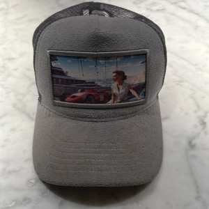 Blå froté keps från Revenite - Säljer en blå froté keps från Revenite med mesh på baksidan och justerbar snapback. Framsidan har en mjuk yta och ett tryckt motiv med bil och är Monaco med en kvinna på, det finns inte och köpa längre från vanliga hemsidan 
